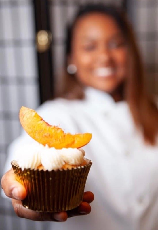 Chef Za'Mecca holding a peach-topped signature cupcake